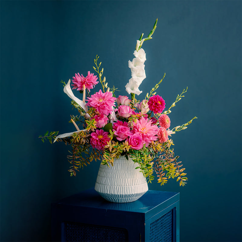 Floral arrangement in a white vase on a blue surface with a dark blue background