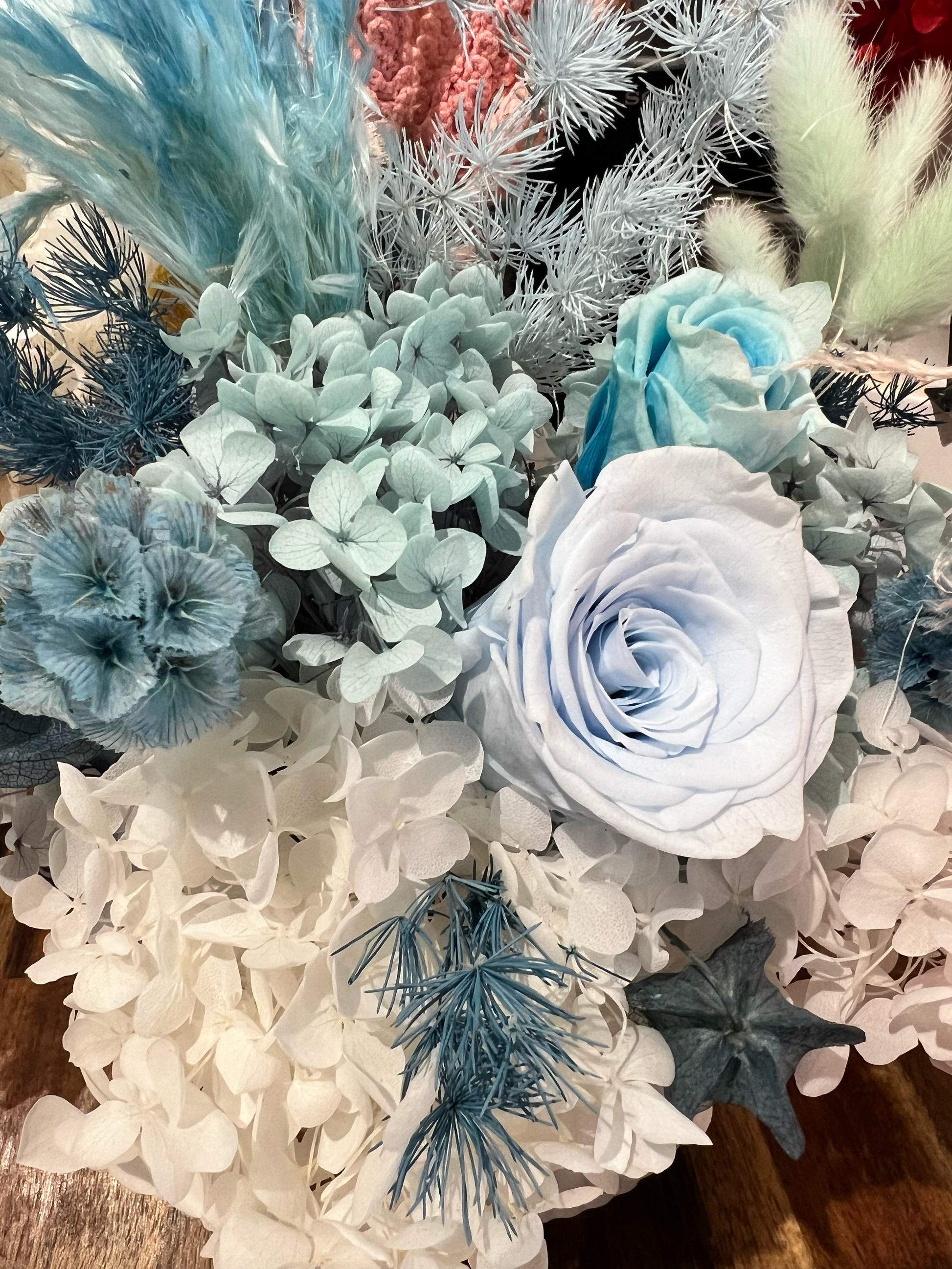 Preserved blue roses with blue and white hydrangeas and complementary blue everlasting flowers, showcasing premium preserved floral materials for floral design.